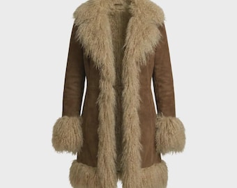 May include: A brown suede coat featuring a long, shaggy beige fur trim along the front opening, collar, cuffs, and hemline. The coat has a structured silhouette with a smooth, matte finish on the suede body and a textured, voluminous fur trim.