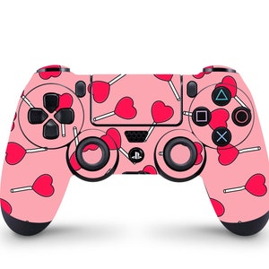 May include: A pink games console controller featuring a pattern of red heart-shaped lollipops. The controller has black buttons and joysticks, with the PlayStation logo in the centre. The controller is designed for a gaming console.