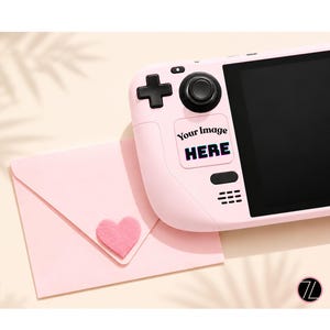 May include: A light pink handheld gaming console featuring a black screen, a directional pad, and a joystick. A rectangular sticker on the device displays the text "Your Image HERE". Beside the console is a light pink envelope with a felt heart.