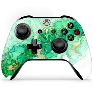May include: A white Xbox controller with a green and gold abstract design. The controller has black buttons and a black D-pad.