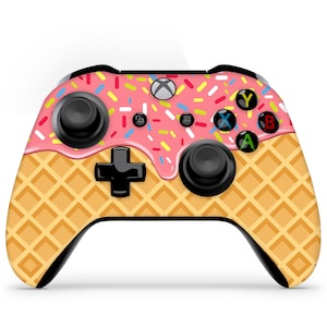 Könnte beinhalten: Ein schwarzer Xbox-Controller mit einem rosafarbenen und weißen Waffelkegel-Design. Der Controller hat ein rosafarbenes und weißes Eiscreme-Design mit Streuseln oben drauf.