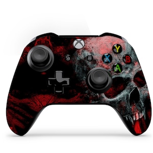 May include: An Xbox controller with a skull design. The controller features a black base with a red and gray skull graphic. The buttons are colored green, blue, yellow, and red. The controller has two joysticks and a directional pad.