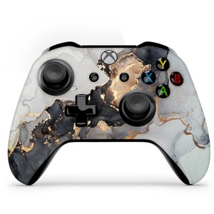 May include: A black and white Xbox controller with a gold marble design. The controller has black buttons and a black d-pad.