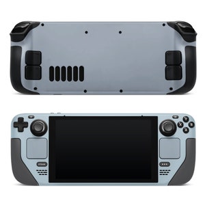 May include: A grey handheld gaming device with a black screen, black buttons, and a black joystick. The device has a grey back panel with black buttons and a black speaker grill.