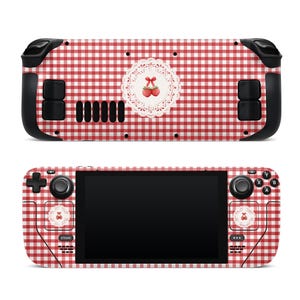 May include: A red and white checkered Steam Deck handheld gaming console skin. The skin features a cherry design on the front and back. The console has black buttons and a black screen.