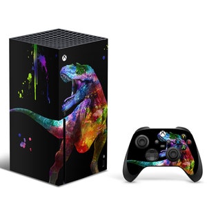 以下が含まれることがあります： カラフルな恐竜のデザインが施された、黒いXbox Series X本体とコントローラー。恐竜はピンク、ブルー、グリーン、イエロー、オレンジの鮮やかなミックスです。