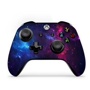 May include: A black Xbox controller with a galaxy-themed design. The controller features a dark blue and purple background with white and pink stars and nebulae.
