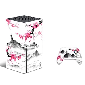 Pode incluir: Um console Xbox Series X branco com um design de cerejeira em flor preto e rosa. O console está ao lado de um controlador Xbox branco com o mesmo design.