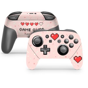 May include: Pink Nintendo Switch controller skin with a pixelated heart and the text "GAME OVER" in a retro video game style.