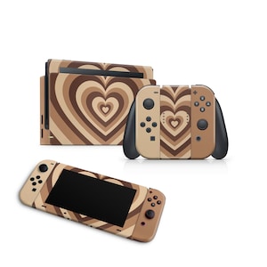 Peut inclure: Une console et une manette Nintendo Switch de couleur beige et marron avec un motif en forme de cœur. Le motif est composé de cercles concentriques qui créent un effet tourbillonnant.