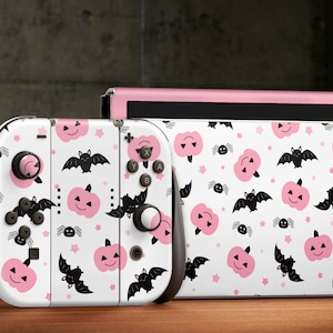 May include: A pink and white Nintendo Switch console and controller with a Halloween-themed design featuring pink pumpkins, bats, and spiders.