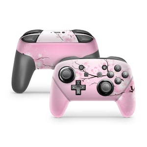 May include: Pink Nintendo Switch Joy-Con controller with a floral design featuring a branch of cherry blossoms. The controller has black buttons and joysticks.