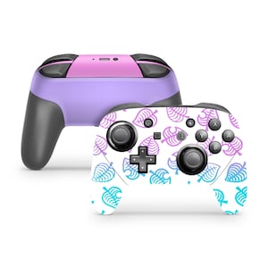 May include: A purple and pink Nintendo Switch controller with a white skin featuring a blue and purple leaf pattern. The controller has the letters A, B, X, Y, and a directional pad.