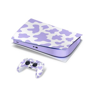 Puede incluir: Una consola y un mando de videojuegos con estampado de vaca, en morado y blanco.