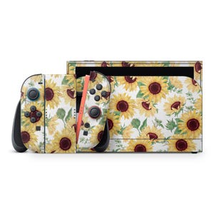 Puede incluir: Una consola Nintendo Switch y sus mandos están decorados con un estampado de girasoles. El diseño presenta girasoles amarillos con centros marrones y hojas verdes sobre un fondo blanco. Los mandos tienen detalles en negro y raíles naranjas.