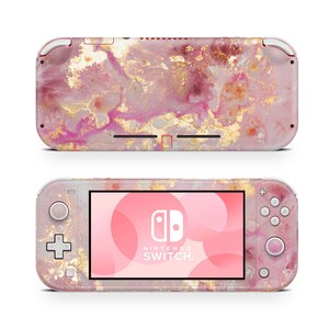 May include: A pink and gold Nintendo Switch Lite console with a marble pattern. The console has a pink and gold design with a white Nintendo Switch logo on the screen.