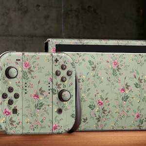 May include: A green Nintendo Switch console and Joy-Con controllers with a floral pattern. The console and controllers are on a wooden surface.