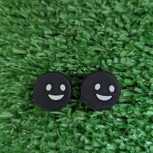 May include: Two black ghost-shaped phone charms with white smiling faces on a green artificial grass background.