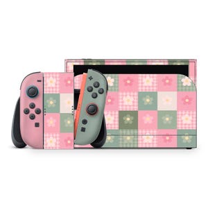 Puede incluir: Una consola Nintendo Switch rosa y verde con mandos Joy-Con a juego. La consola y los mandos presentan un estampado floral con cuadrados rosas, verdes y blancos. Los Joy-Cons son rosas y verdes con botones negros.