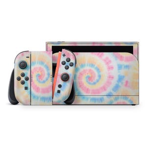 Puede incluir: Una consola Nintendo Switch y mandos Joy-Con con un diseño tie-dye. Los mandos son blancos y negros con un patrón en espiral en tonos rosa, amarillo y azul. La consola tiene un patrón tie-dye a juego.