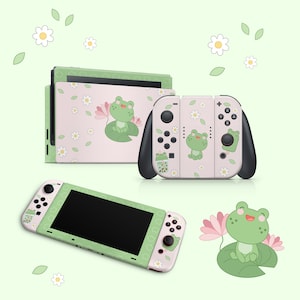 May include: A green and pink Nintendo Switch console and two controllers with a frog and flower design. The console and controllers have a pink background with green frogs, flowers, and leaves.