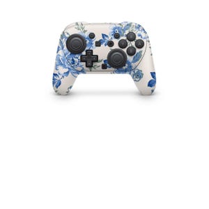 Może przedstawiać: Biały kontroler do gier z niebieskim kwiatowym wzorem. Kontroler ma czarne przyciski i joysticki. Kwiatowy wz&oacute;r przedstawia niebieskie kwiaty i liście.