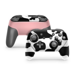 May include: A black and white cow print Nintendo Switch controller. The controller has a black and white cow print design with black buttons and a black joystick.