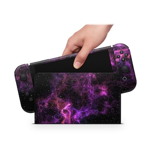 Könnte beinhalten: Eine Nintendo Switch Konsolenhaut im Galaxie-Design in Lila und Schwarz. Die Haut zeigt ein wirbelndes Nebelmuster in Rosa- und Lilatönen.