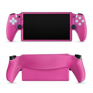 May include: A pink handheld gaming console with a black screen and integrated controllers. The controllers feature white buttons and directional pads. The console is shown from two angles, top and side.