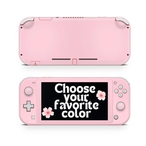 May include: A pink Nintendo Switch Lite handheld gaming console with a white button and a white screen. The screen displays the text "Choose your favorite color" with a pink flower graphic on either side of the text.
