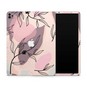 May include: A pink and beige iPad case with a floral design and abstract shapes. The case has a black Apple logo on the front.