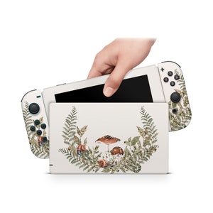 Pode incluir: Pele de console Nintendo Switch branca com um design de aquarela de cogumelos, samambaias e caracóis. O design é centralizado na consola e tem um fundo branco.