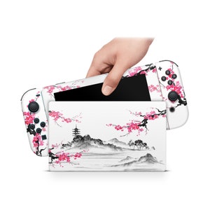 May include: White Nintendo Switch console with a custom skin featuring a Japanese-inspired design of a pagoda, mountains, and cherry blossoms in pink and black ink.