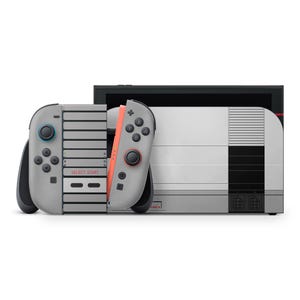 May include: A gray Nintendo Switch console and controllers with a retro NES design. The controllers have gray buttons and a coral-colored side. The console has a white and gray design with black accents. The text "SELECT START" is visible on the controller.