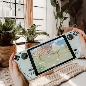 Può includere: Una console per videogiochi portatile verde chiaro con uno schermo bianco che mostra il gioco "Wild Flowers". La console ha un joystick e pulsanti neri. Il menu del gioco mostra le opzioni "Carica gioco", "Impostazioni" e "Esci".