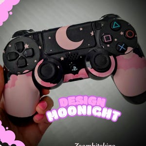 May include: A black PlayStation 4 controller with a pink and black moon and stars design. The controller has a pink and black cloud design on the handles. The text "DESIGN MOONIGHT" is in pink letters on a black background. The text "Zoomhitskins" is in white letters on a black background.