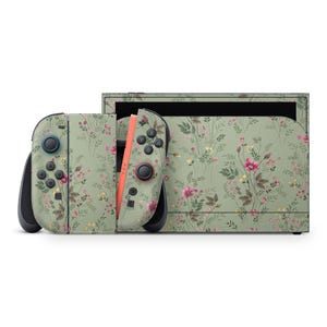 Puede incluir: Una consola Nintendo Switch y mandos Joy-Con con un diseño floral. Los mandos tienen un fondo verde claro con flores rosas y amarillas. La base de la consola tiene un patrón floral a juego.