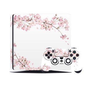 Puede incluir: Una consola PlayStation 4 blanca y un mando con un diseño de flores de cerezo rosas. La consola y el mando están cubiertos por un patrón floral.