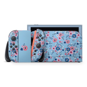 May include: A light blue Nintendo Switch console and controllers with a floral pattern of pink, blue, and white flowers. The console and controllers are on a white background.
