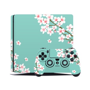 May include: A teal and white PlayStation 4 console and controller with a cherry blossom design. The console and controller are both decorated with a delicate pattern of pink cherry blossoms on a light teal background.