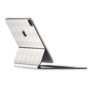 May include: An Apple iPad Pro with a light beige and white plaid pattern on the back and keyboard cover. The Apple logo is visible on the back of the tablet. The keyboard is attached and folded open.
