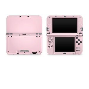 May include: A pink Nintendo 3DS handheld games console, displayed open and closed. The open console shows two black screens, with the bottom screen featuring a directional pad and buttons. The closed console shows the exterior with a smooth, matte finish.