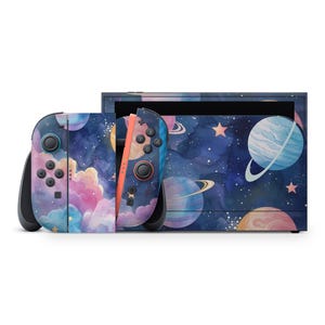 May include: A Nintendo Switch console and Joy-Con controllers feature a space-themed design. The controllers have a watercolor design with planets, stars, and clouds in shades of blue, purple, and pink. The console has a matching design.