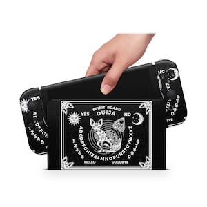 May include: Black and white Ouija board-themed Nintendo Switch case. The case features a stylized cat illustration, sun, moon, and star designs, and the words "Spirit Board", "Ouija", "Hello", and "Goodbye".