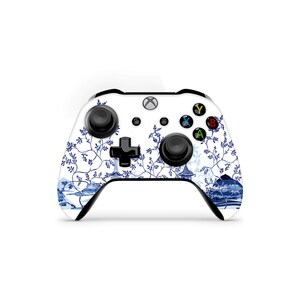 May include: A white Xbox controller with a blue and white floral design. The controller has black buttons and a black D-pad.