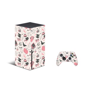 May include: A white Xbox Series X console and controller with a pink and black Halloween-themed design. The design features cats, pumpkins, skulls, and other spooky elements.