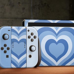 May include: A blue and white Nintendo Switch console and controller with a heart-shaped pattern. The console and controller are both decorated with a swirling, concentric heart design.