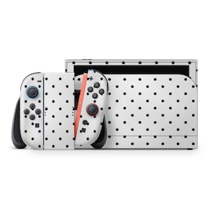 May include: A white Nintendo Switch console and controllers with a black polka dot pattern. The controllers have black buttons and joysticks, with one controller featuring a coral-colored rail. The screen has a black border.