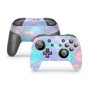 May include: A wireless video game controller featuring an iridescent opal-inspired pattern with soft pastel hues of pink, blue, and purple. The controller includes black analog sticks, a directional pad, and standard action buttons labeled A, B, X, and Y.