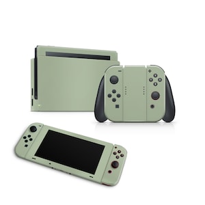 Op de afbeelding: Een sagegroene Nintendo Switch-console met bijpassende Joy-Con-controllers. De console bevindt zich in de handheld-modus met een zwart scherm. De Joy-Con-controllers zijn aan de zijkanten van de console bevestigd.